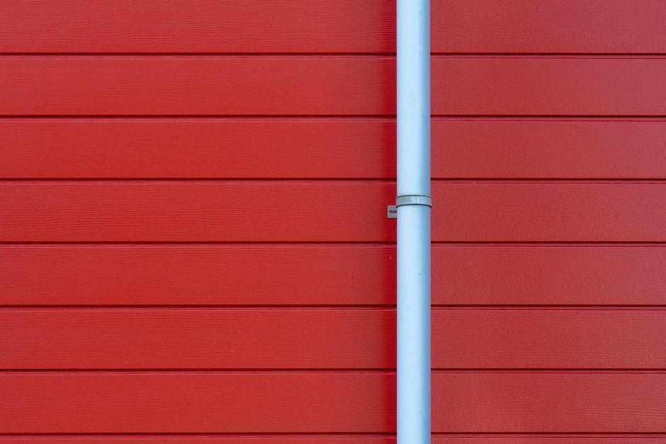Grey downpipe fixed to a red-painted timber-clad wall